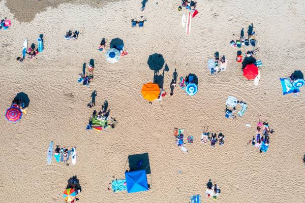aerial shot of people on beach, there are brightly colored umbrellas dotted along the sand