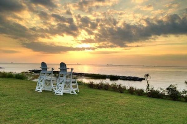 two empty chairs on grassy hill facing the water at sunset