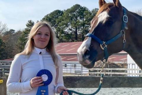 woman posing with a horse and a blue ribbon for first place in an equestrian competition