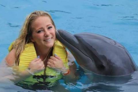 woman in yellow life jacket in water with a bottle nose dolphin